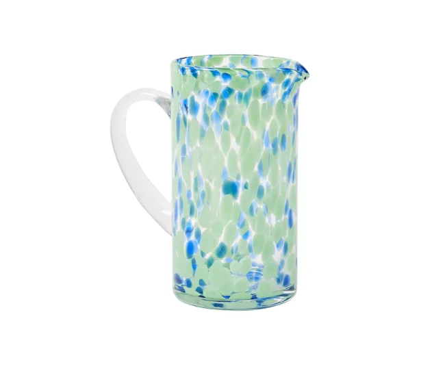 Glass pitcher with green and blue speckled pattern and a white handle on a plain background.