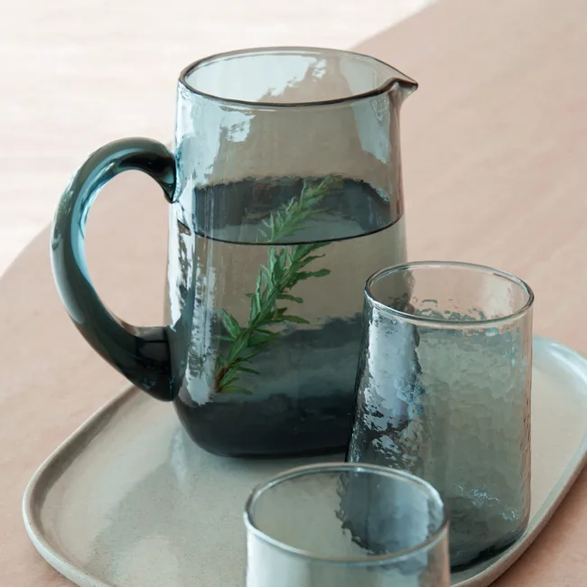 A blue glass pitcher with sprig, two glasses, and a tray on a light surface.
