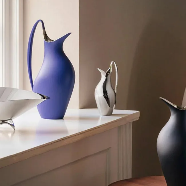 Sleek modern pitchers and a bowl on a light-colored shelf with natural lighting from a nearby window.