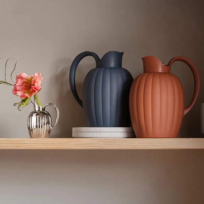 Decorative shelf with a silver pitcher holding a pink flower, and two large, ribbed pitchers in blue and terracotta.