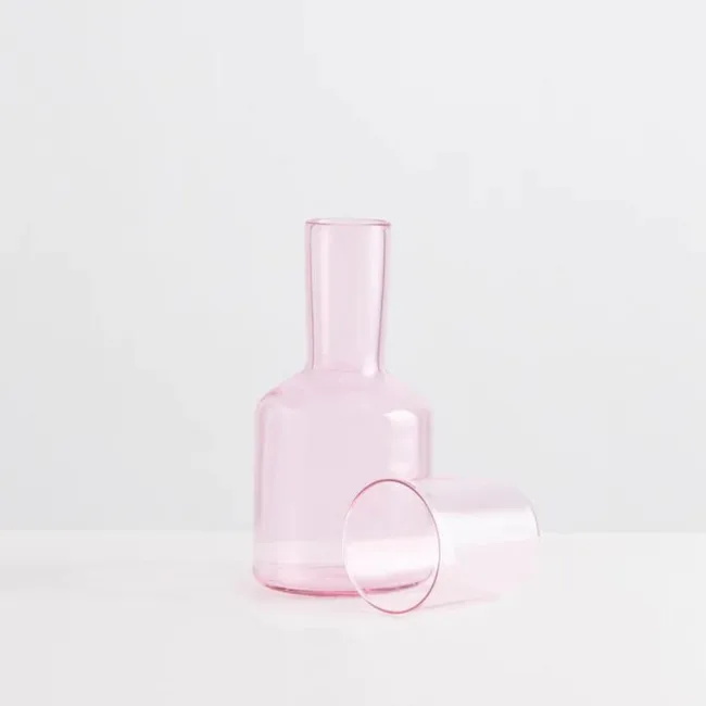 A pink glass carafe with a matching glass on a white surface.