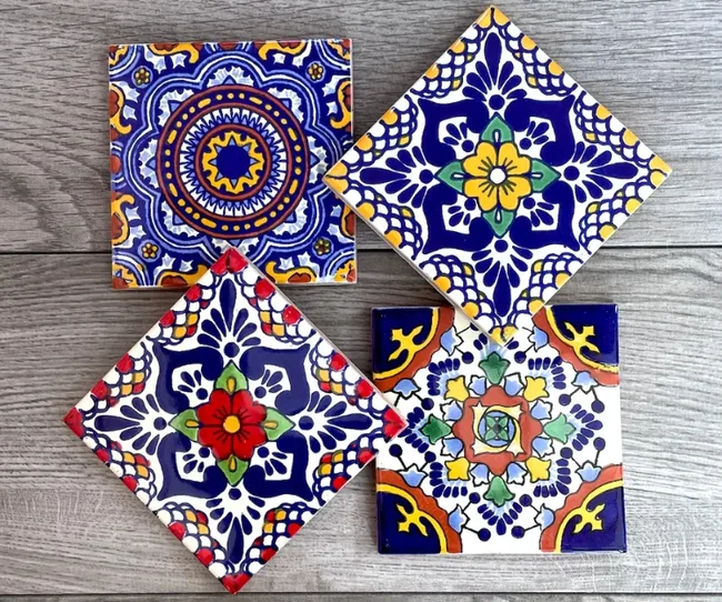 Four colorful, intricately patterned ceramic tiles on a wooden surface.