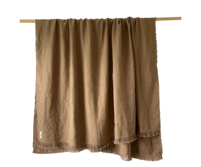 Brown linen throw draped on a wooden rod, featuring a fringed edge at the bottom.