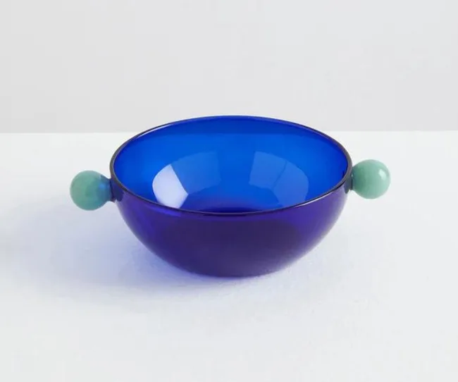 Blue glass bowl with teal spherical handles on each side, placed on a white surface.