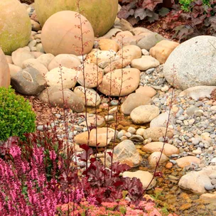 Garden with round stones, small stream, and pink flowers in the foreground.