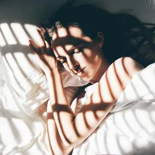 Person sleeping peacefully in bed, light and shadow patterns on face and body.