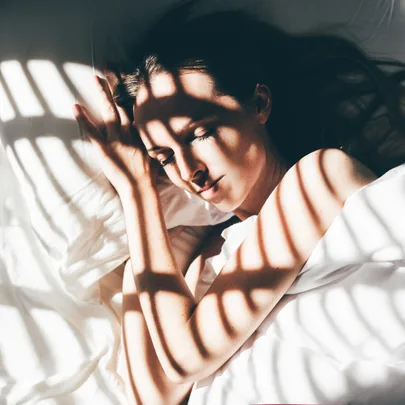 Person sleeping peacefully in bed, light and shadow patterns on face and body.