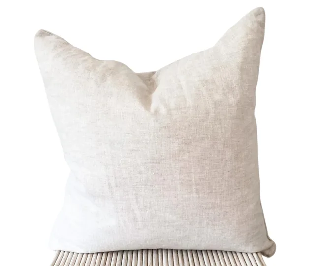 Beige linen pillow on a rattan chair, showcasing a simple, elegant design.