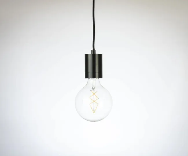 Hanging light bulb with a black fixture against a plain background.