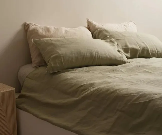 A neatly made bed with green and beige linen pillows and covers in a softly lit room.
