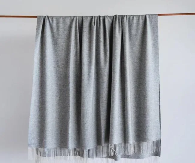Gray cashmere throw draped over a wooden rod, featuring fringe details at the bottom.