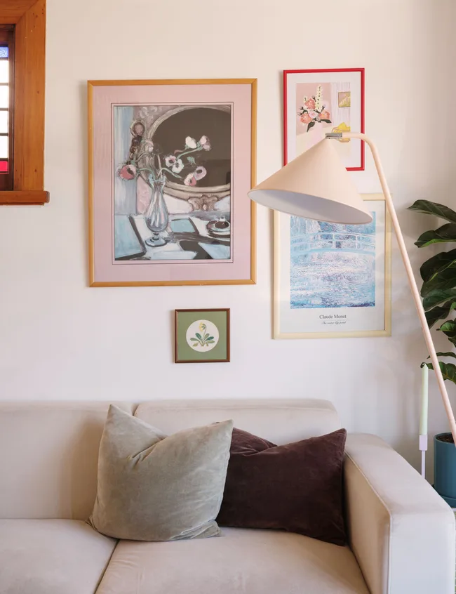 Living room with wall art, a floor lamp, and a beige couch with two pillows.