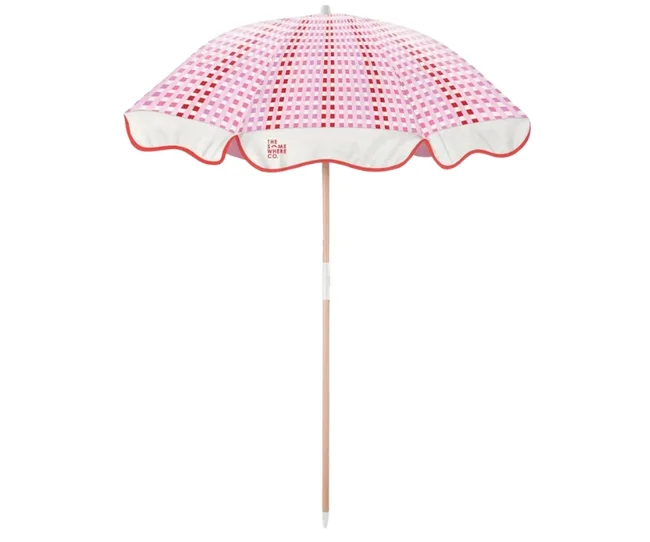 Pink and red checkered beach umbrella with a scalloped edge on a wooden pole.