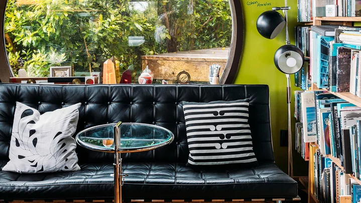 Cozy room with round window, black sofa, glass table, patterned cushions, and bookshelves filled with books.