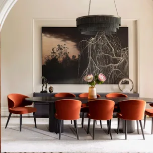 Dining room with orange chairs, dark oval table, large wall art, and a pendant light above.