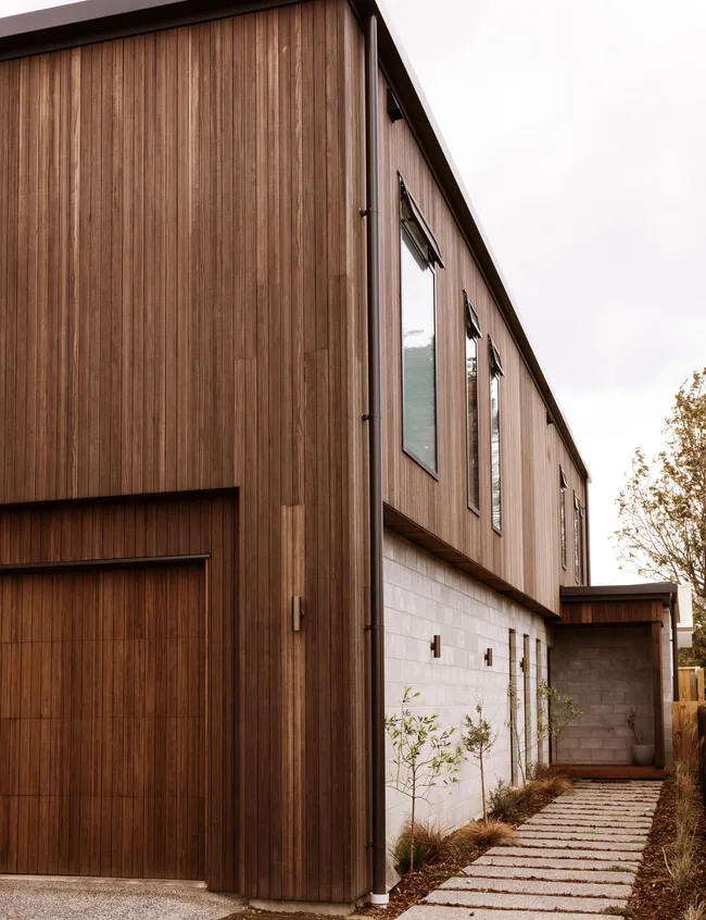 Modern two-story house with wood siding, large windows, and a stone walkway leading to the entrance.