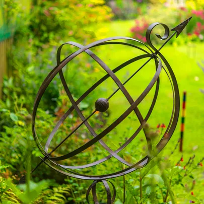 Armillary sphere sculpture in a vibrant garden setting with green grass and colorful flowers in the background.
