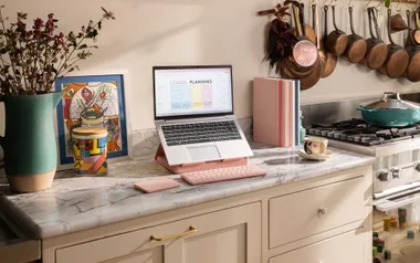 Laptop on kitchen counter with pink keyboard, vase, framed art, and cookware.