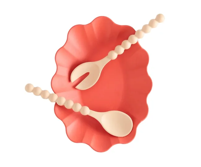 Red scalloped serving bowl with two beige serving utensils on top.