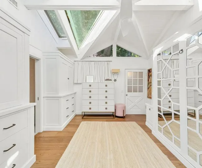 Bright white room with skylights, wooden floor, dresser, and mirrored closet doors.