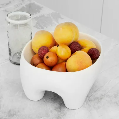 Bowl of peaches, raspberries, and loquats on a marble surface with a glass of water.