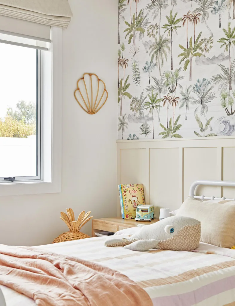Cozy children's bedroom with palm-themed wallpaper, plush whale toy on bed, and illustrated book on the nightstand.