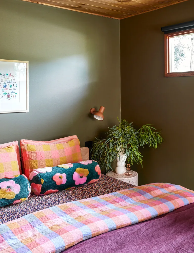 Cosy bedroom with colourful checked bedding, floral pillows, green walls, and a small window.