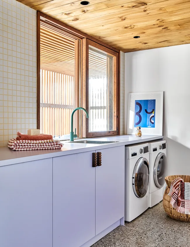Laundry room with modern washer, dryer, purple cabinets, wicker basket, and folded towels on countertop.