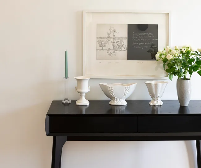 Decorative black table with white vases, green candle, framed artwork, and a vase of white roses.