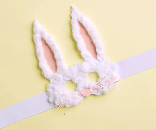White fluffy bunny mask with pink inner ears on a yellow background.