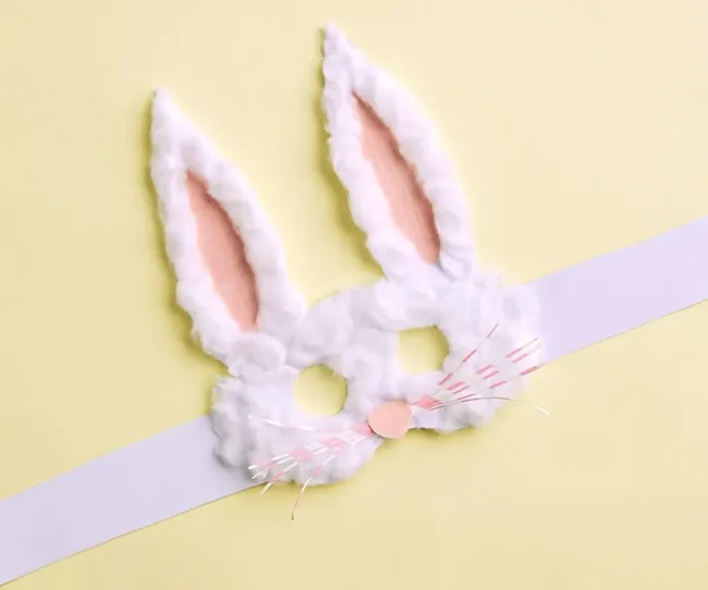 White fluffy bunny mask with pink inner ears on a yellow background.