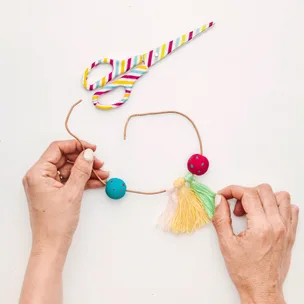 Crafting a colorful necklace with tassels and beads; striped scissors in the background.