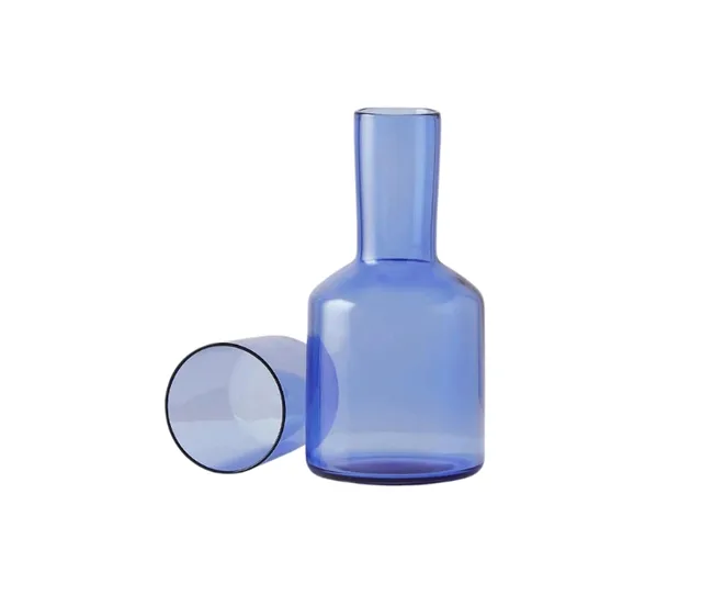 Clear blue glass carafe with matching glass cup lying beside it on a white background.