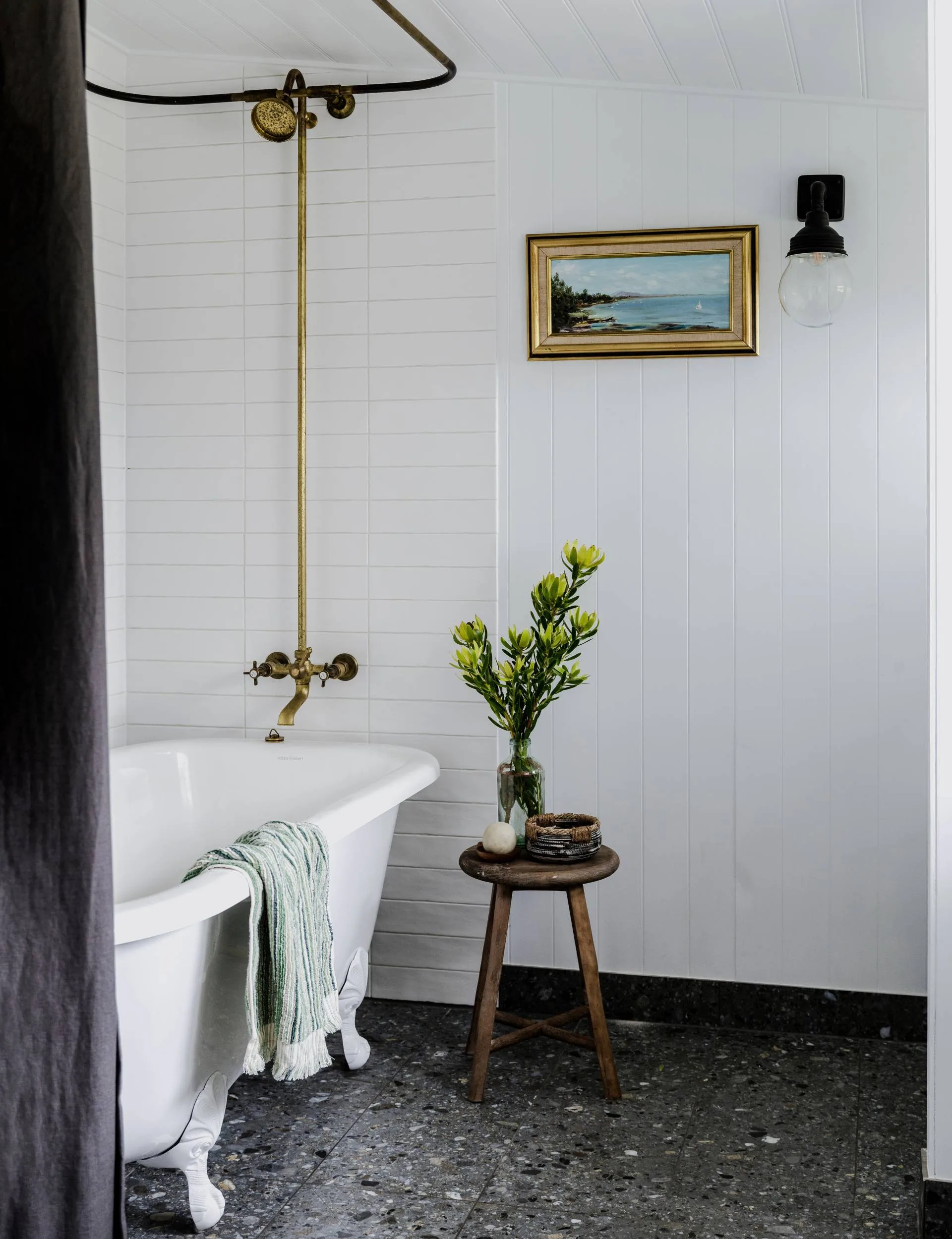 A white tiled bathroom with a claw foot tub and shower curtain