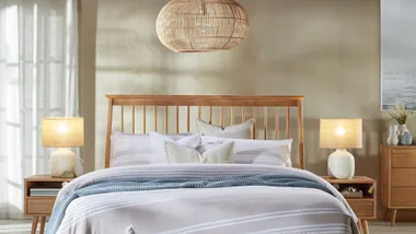 Bedroom with wooden bed, striped bedding, wicker basket, rattan light fixture, and side tables with lamps.