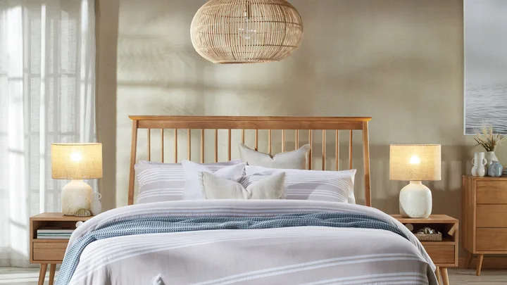 Bedroom with wooden bed, striped bedding, wicker basket, rattan light fixture, and side tables with lamps.