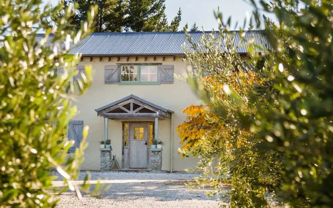 Charming house with rustic door and shutters, surrounded by greenery and trees in the foreground.