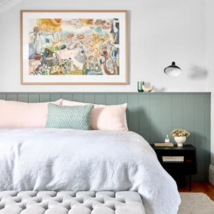 A cozy bedroom with a large colorful abstract painting above the bed and a modern tufted bench at the foot of the bed.