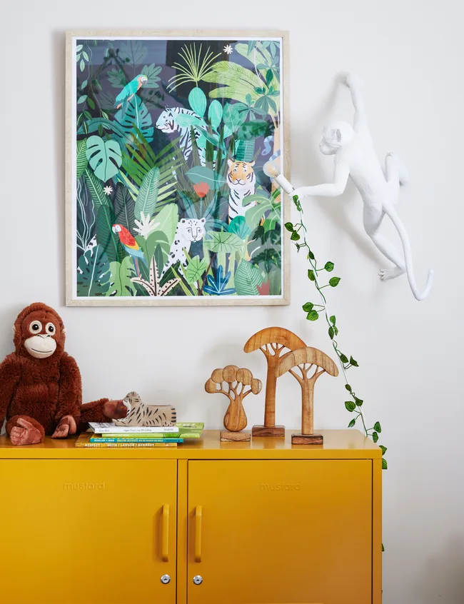 Yellow cabinet with a jungle-themed framed artwork, monkey wall light, plush orangutan, and wooden trees.