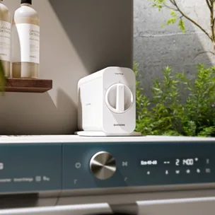 Samsung SmartThings Air Purifier on a washing machine with eco detergent bottles on a shelf in a bright laundry room.