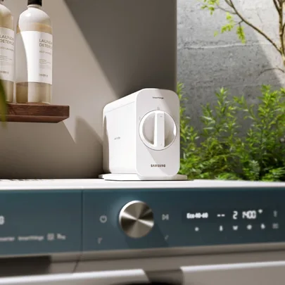 Samsung SmartThings Air Purifier on a washing machine with eco detergent bottles on a shelf in a bright laundry room.
