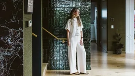 A woman wearing white shirt and pants against a wall of green tile