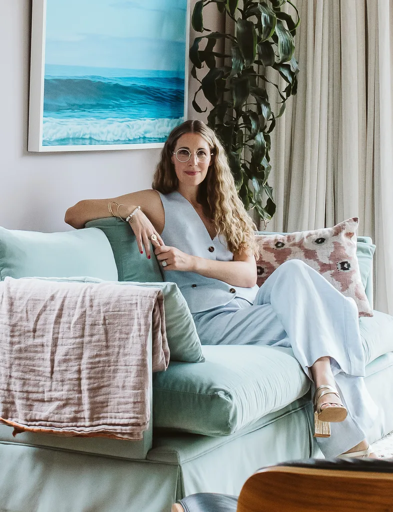A woman wearing a blue outfit sitting on a blue sofa with a wave print behind her.