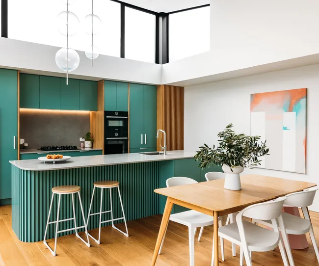 Modern kitchen and dining area with teal cabinets, wood accents, and a light-filled space with abstract wall art.
