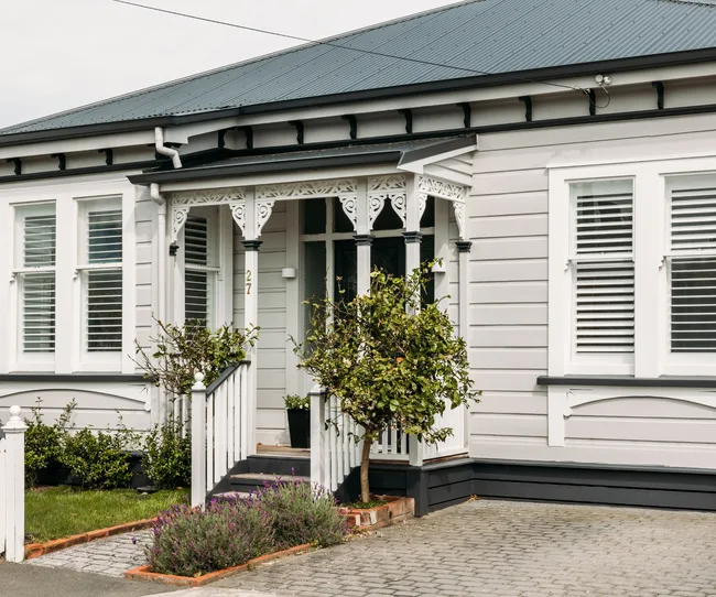 A charming, white single-story house with decorative trim, a small porch, and a well-maintained front garden.