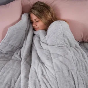 A person sleeps peacefully under a soft, gray blanket, with light pink pillows in the background.