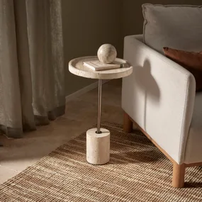 A small round side table with a marble texture holds a book and sphere, next to a light gray sofa on a woven rug.