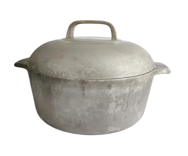 Vintage aluminum pot with lid and handle, showing signs of wear.