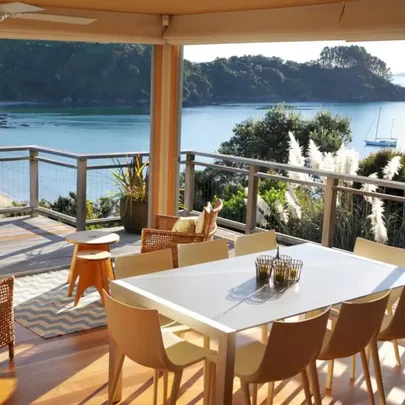 Outdoor dining area with a white table and chairs overlooking a scenic bay and lush greenery.