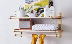 Laundry room with shelf holding artwork, towels, watering can, and bottles; yellow socks hanging below.